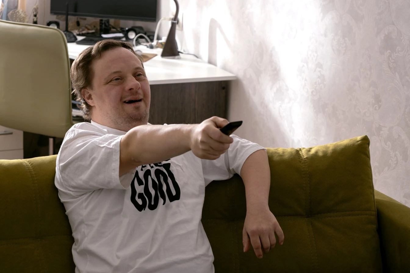 Man with down syndrome sitting on couch and smiling while using TV remote