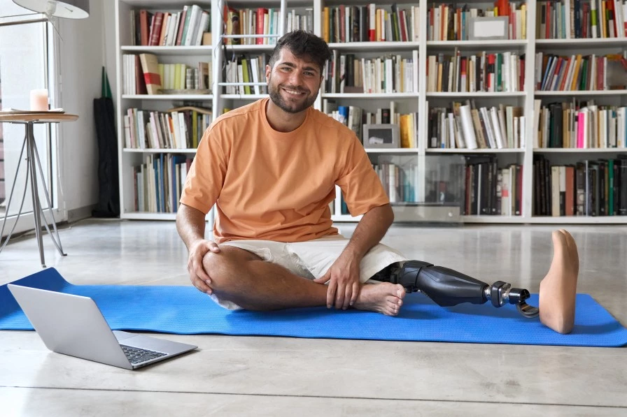 Disabled man sitting on pilates mat with laptop set up to enjoy online class