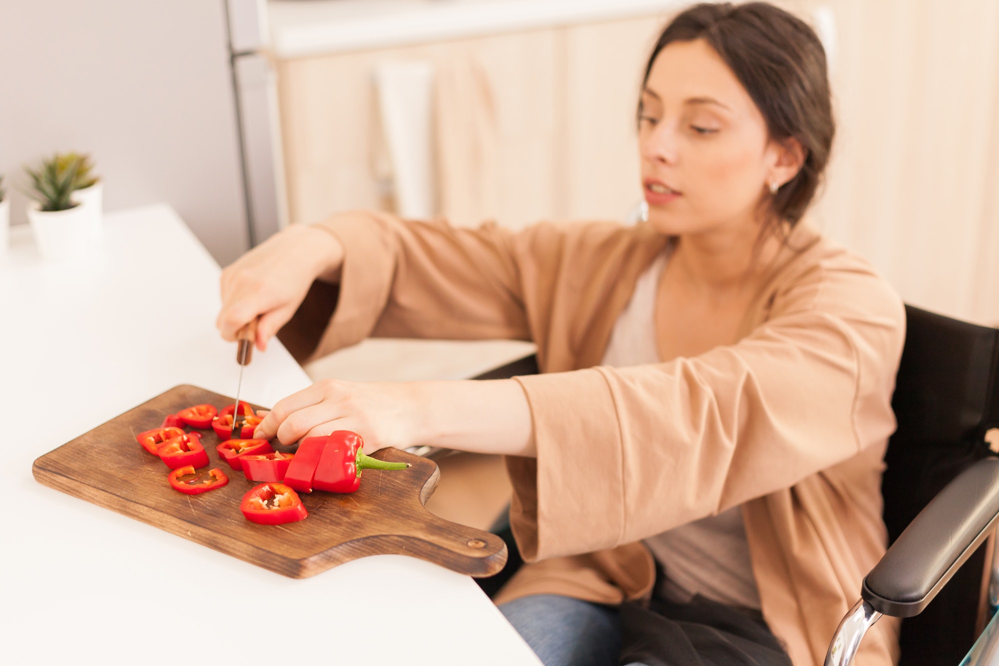 Woman in wheelchair cutting capsicum at kitchen table