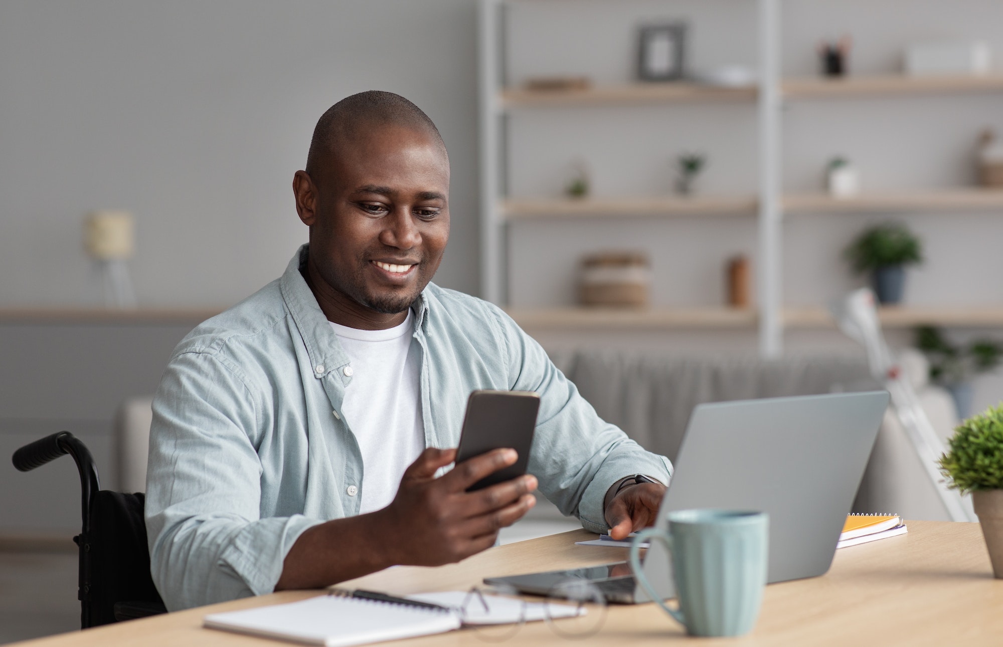 Man smiling in wheelchair sitting at desk using laptop and making phone call